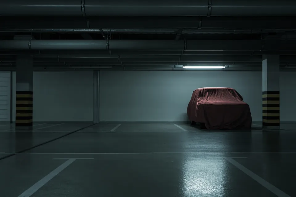 Dark parking garage, empty except for one car covered with a red tarp